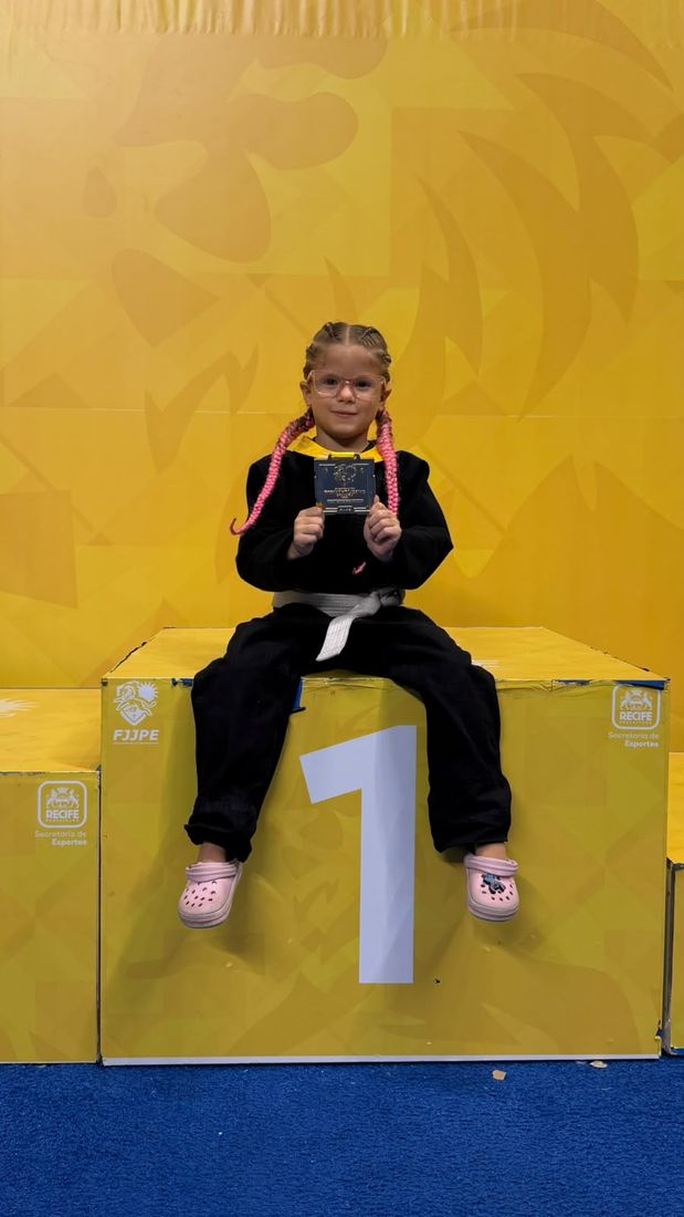 Lorena Veloso sentada no lugar mais alto do pódio segurando a medalha de ouro da 2ª Etapa do Campeonato Pernambucano Kids 2026